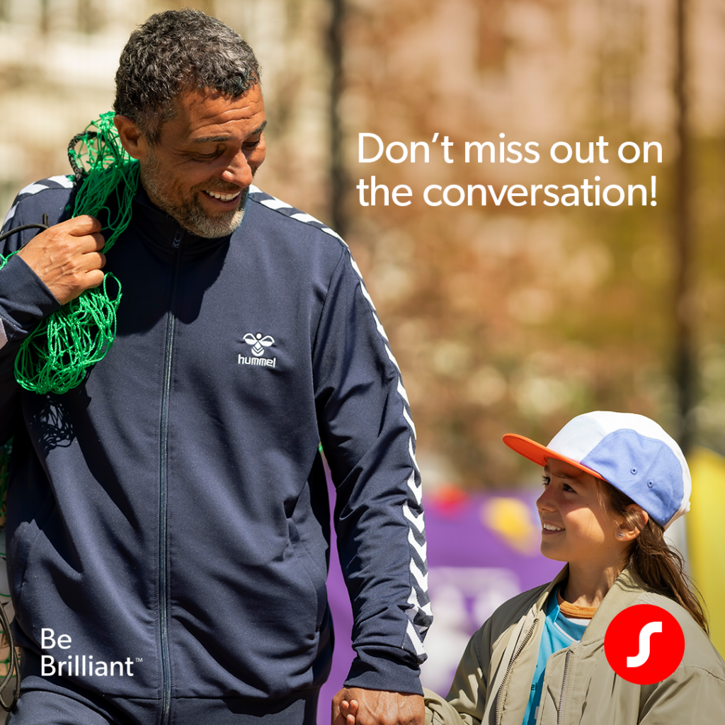 The youth soccer coach in a navy blue hummel track jacket walks outside, holding a green sports net over his shoulder while looking down affectionately at a young child in a blue and white cap. Text reads, 'Don’t miss out on the conversation!' with campaign branding on the bottom corners.