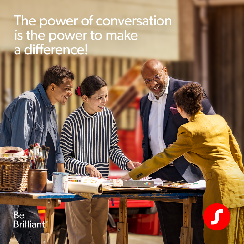 Four professionals stand outdoors gathered around a blue workbench, talking and smiling. Text on the top left reads, 'The power of conversation is the power to make a difference!' The lower left features 'Be Brilliant™' branding, and a Signia logo is in the bottom right corner.