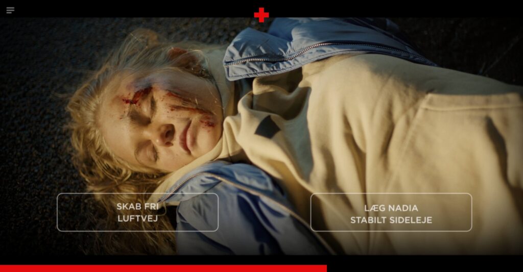 An interactive video frame showing a close-up overhead view of an unconscious blonde girl lying on the asphalt with blood on her face. Two interactive button choices are displayed over her chest: 'SKAB FRI LUFTVEJ' (Create an open airway) on the left, and 'LÆG NADIA STABILT SIDELEJE' (Place Nadia in the recovery position) on the right.