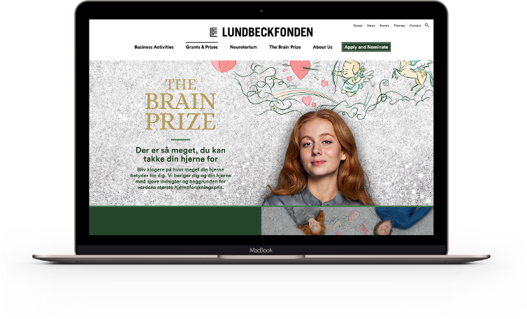 A laptop showing the Lundbeckfonden website homepage with the header 'THE BRAIN PRIZE'. The main banner displays a young woman with long red hair against a textured grey background. Whimsical line drawings of a cupid, a flying horse, and a rainbow emerge like thoughts from her head. Danish text reads, 'Der er så meget, du kan takke din hjerne for' (There is so much you can thank your brain for).