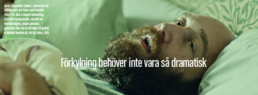 A close-up video still of a bald, bearded man lying in bed with an exaggeratedly miserable expression, looking upward as if suffering intensely. White overlay text across his chest reads 'Förkylning behöver inte vara så dramatisk' (A cold doesn't have to be so dramatic). Small medical disclaimer text from McNeil Sweden AB is visible in the top left corner.